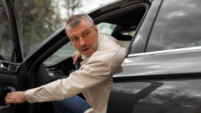 Man in a white shirt leans out the door of a formal car.