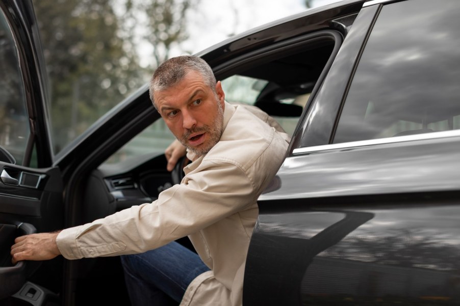 Man in a white shirt leans out the door of a formal car.