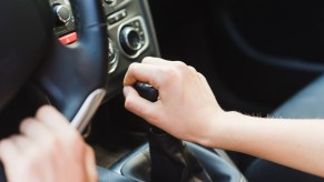 Woman's hand on the gearshift lever of a manual stick shift transmission.