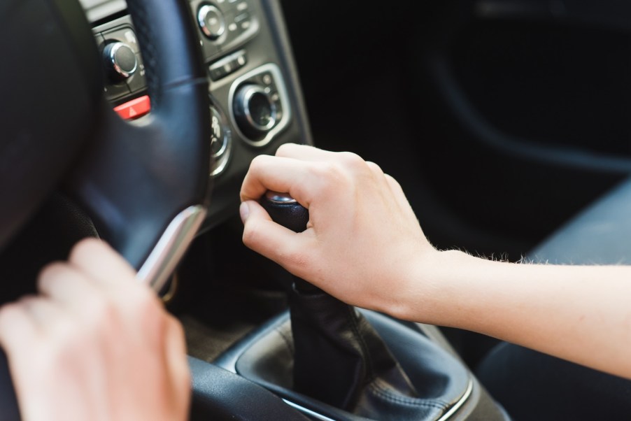 Woman's hand on the gearshift lever of a manual stick shift transmission.