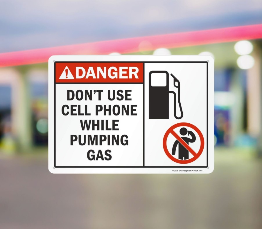 A white sign reads "Danger Don't user cell phone while pumping gas" superimposed on a blurry gas station background.