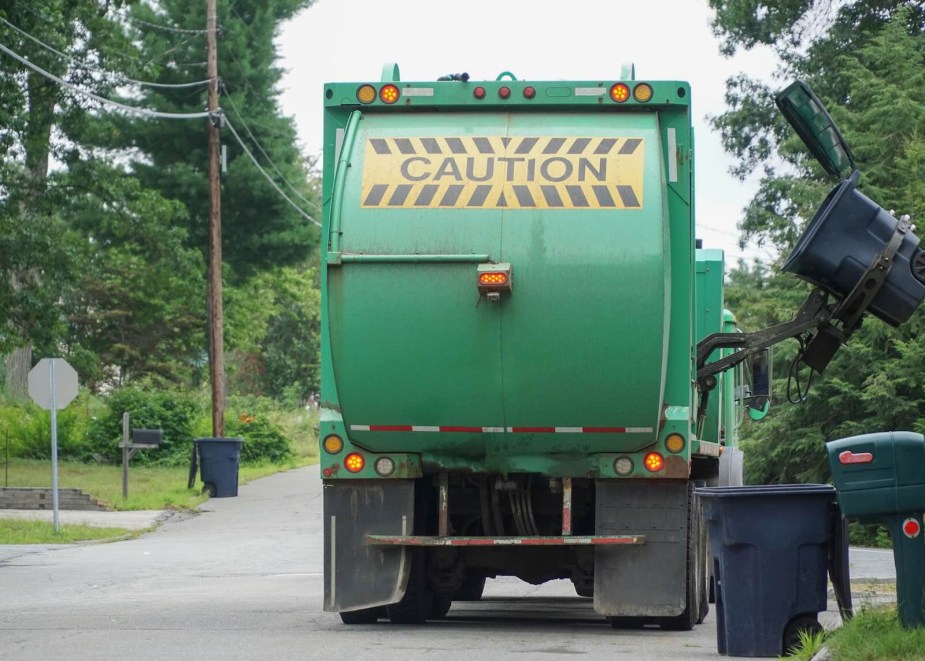 Green recycling truck picks up a bin on a residential street.