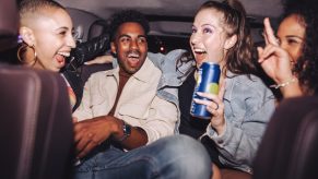 Passengers in the back seat of a car, drinking and laughing.