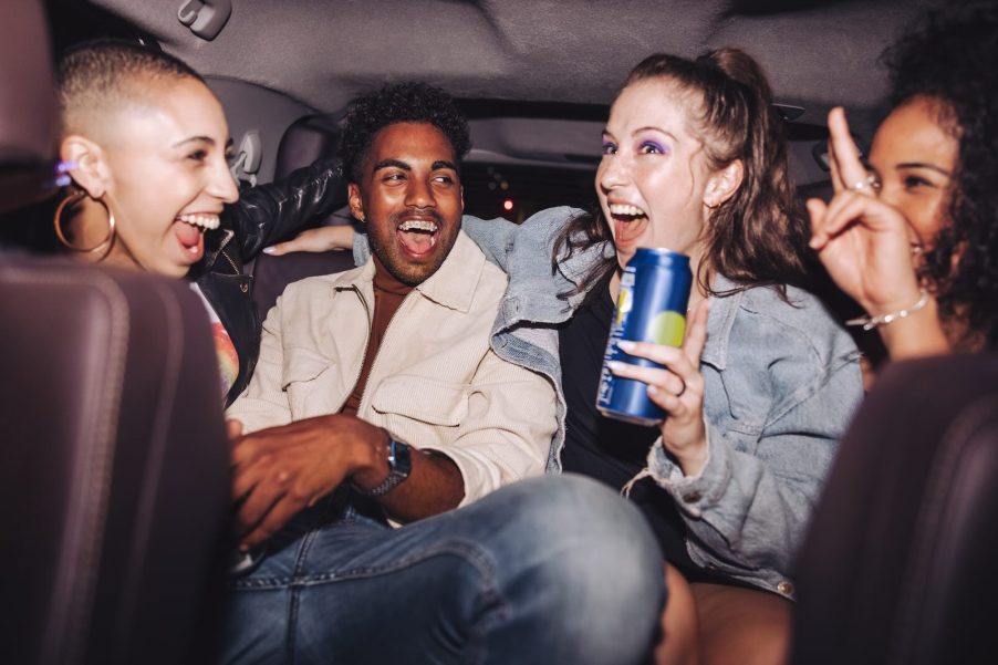 Passengers in the back seat of a car, drinking and laughing.