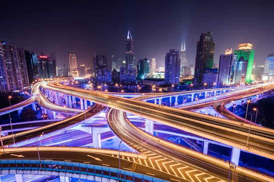 Highway overpasses above a city full of purple street lights, skyscrapers visible in the background.