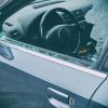 A criminal vandalizing a car smashes the driver's side windows.