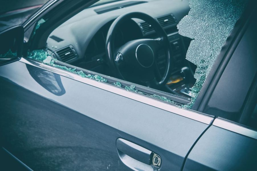 A criminal vandalizing a car smashes the driver's side windows.