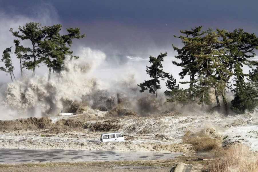 Kei-class van swept out to sea in Japanese Tsunami, trees visible on the shore in the background.