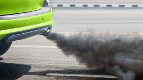 A bright green car burns oil black smoke tailpipe in close view