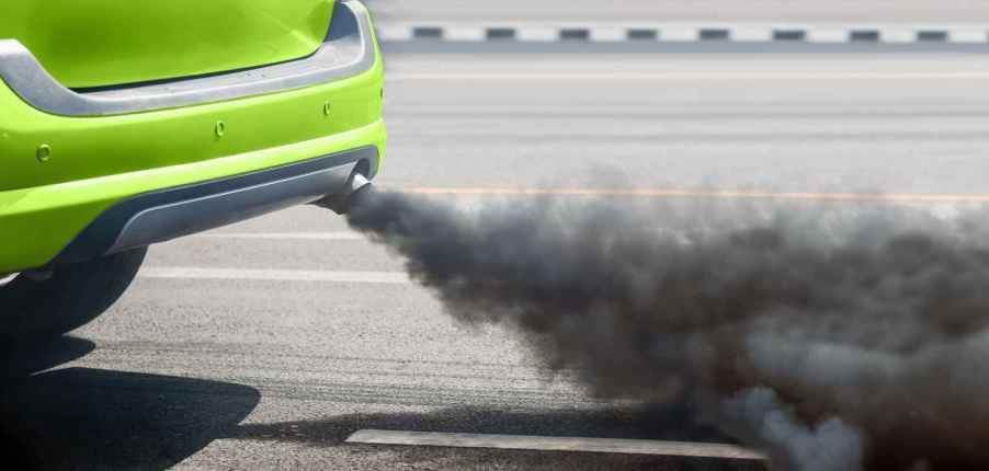 A bright green car burns oil black smoke tailpipe in close view