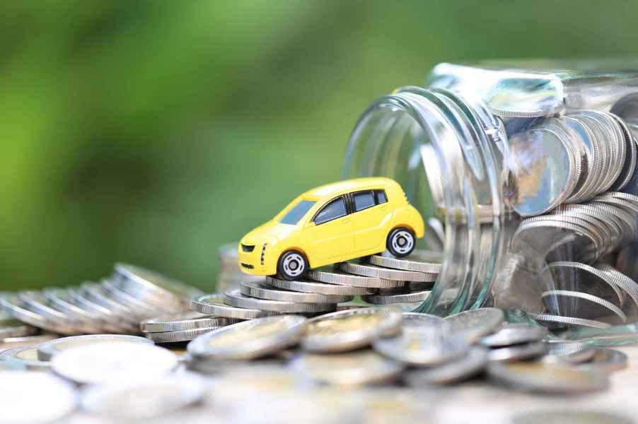 A toy car perched on an overturned jar of silver coins depiction of car insurance costs