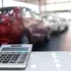 A blurred car dealership showroom with a desk calculator in the foreground to depict a car payment