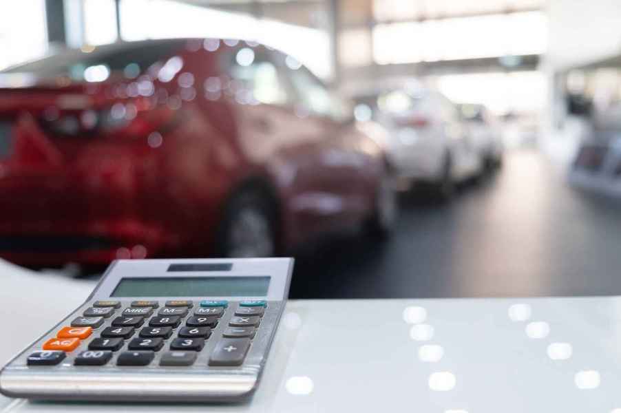 A blurred car dealership showroom with a desk calculator in the foreground to depict a car payment