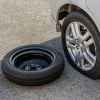 A donut wheel laying next to a flat tire on a car in close view