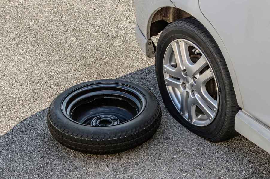 A donut wheel laying next to a flat tire on a car in close view