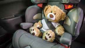 A teddy bear buckled into a child safety seat inside a car