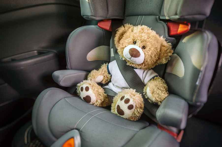 A teddy bear buckled into a child safety seat inside a car