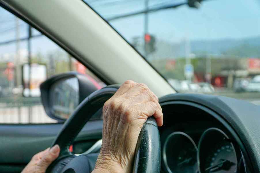 An elderly driver hands shown in close view gripping a car's steering wheel