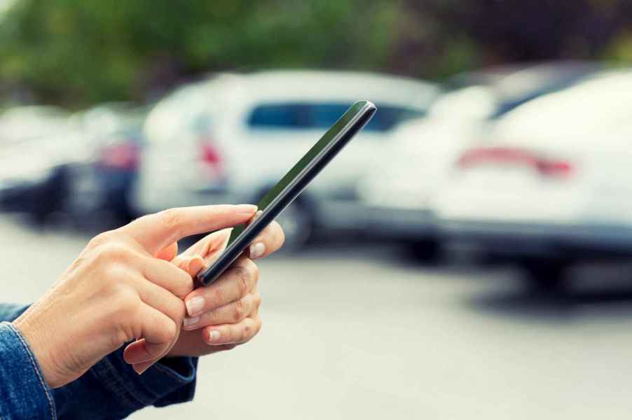 A woman's hands shown holding a cell phone in front of a blurred row of cars parked outside