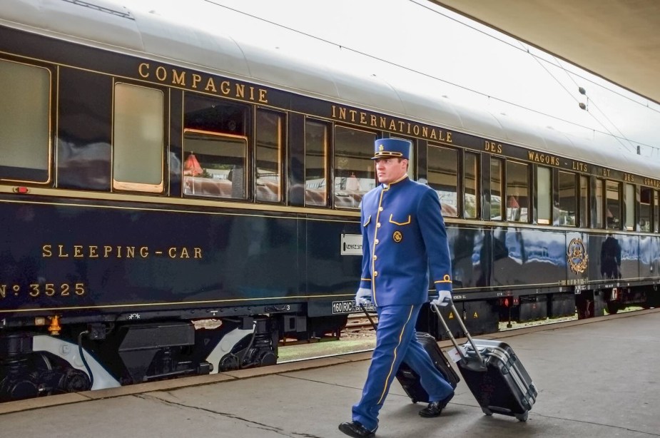 Baggage handler and conductor wheels two pieces of luggage along a platform next to the Orient Express.