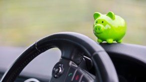 A green piggy bank perched on a car's dash above the steering wheel black interior