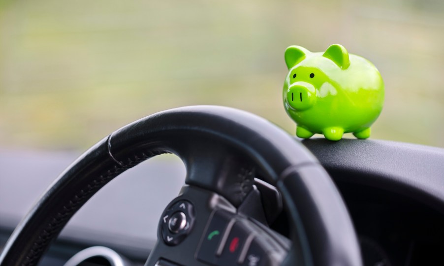 A green piggy bank perched on a car's dash above the steering wheel black interior