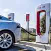 A Tesla EV parked charging at a Tesla Supercharger station in left rear view