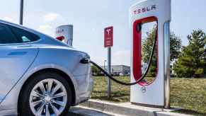 A Tesla EV parked charging at a Tesla Supercharger station in left rear view