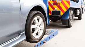 Tow truck towing a silver car in close left front wheel of silver car view