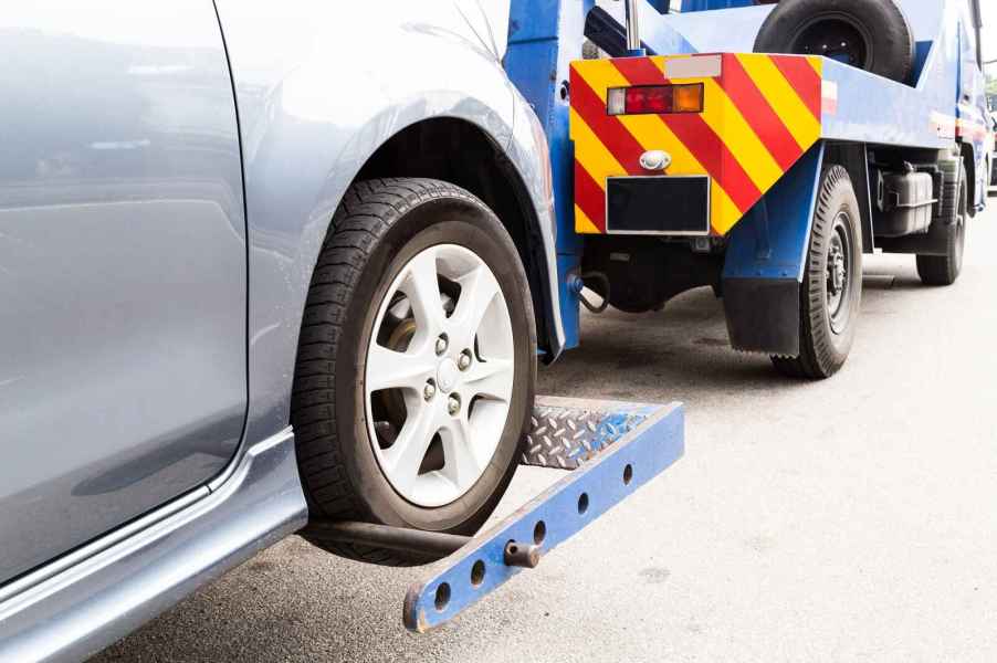 Tow truck towing a silver car in close left front wheel of silver car view