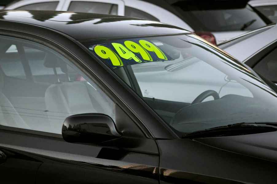 A black used car with price sticker parked at a used car dealer in close view of windshield right front angle