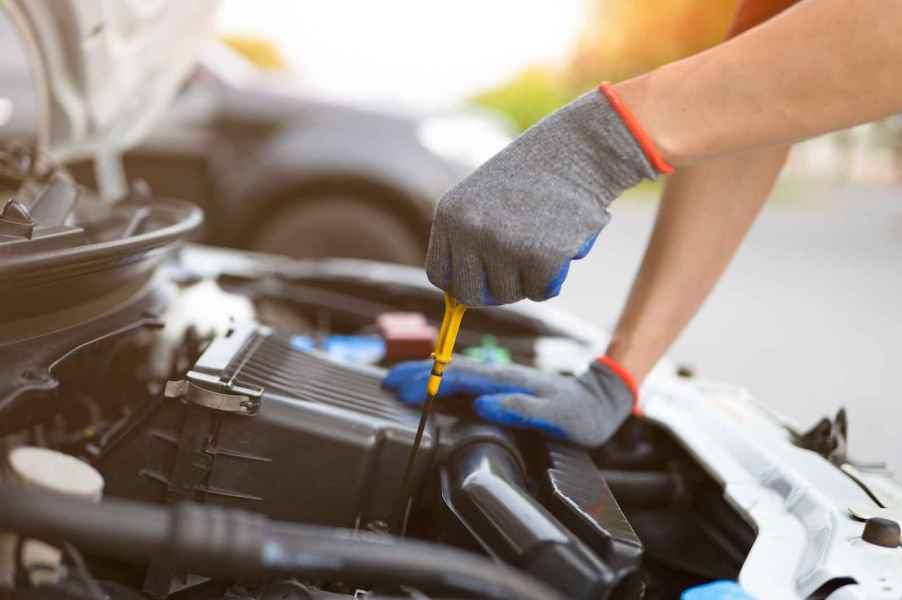 Gloved technician checking a car's engine oil level pulling the dipstick before an oil change in close view