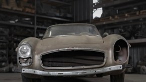 Unpainted Mercedes-Benz 300SL roadster supercar sitting in a barn, missing one headlight and grille.