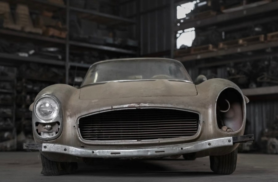 Unpainted Mercedes-Benz 300SL roadster supercar sitting in a barn, missing one headlight and grille.