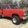 A red 1976 classic Dodge W100 pickup truck parked outside on cement in low right front angle view