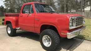 A red 1976 classic Dodge W100 pickup truck parked outside on cement in low right front angle view