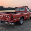 A red 1980 Toyota SR5 Pickup truck parked in right rear angle view with the sun setting in background