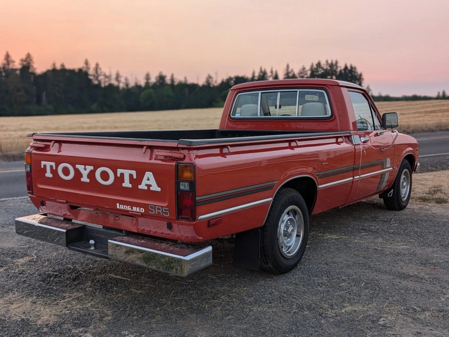 A red 1980 Toyota SR5 Pickup truck parked in right rear angle view with the sun setting in background