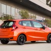 A dark orange 2020 Honda Fit parked in right rear angle view in front of a building with large glass windows