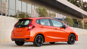 A dark orange 2020 Honda Fit parked in right rear angle view in front of a building with large glass windows