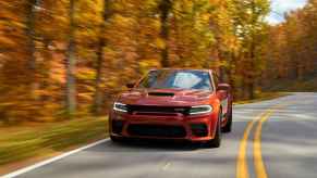 A rust-colored 2023 Dodge Charger Hellcat Redeye Widebody making 807 horsepower driving on a paved two-lane with fall trees in background