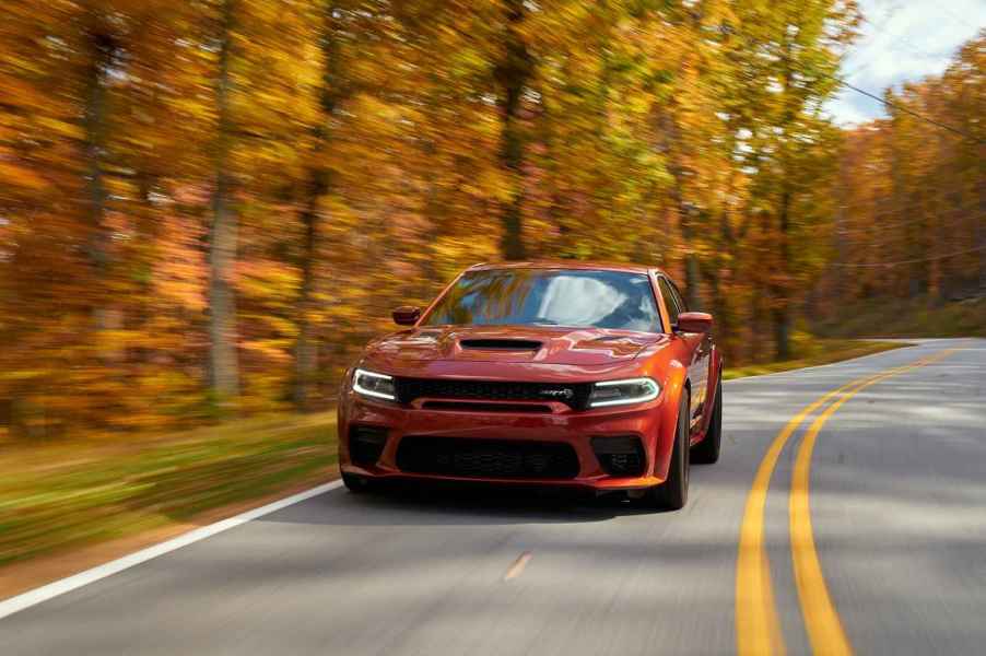 A rust-colored 2023 Dodge Charger Hellcat Redeye Widebody making 807 horsepower driving on a paved two-lane with fall trees in background