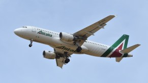 Alitalia airplane flying in front of a blue sky.