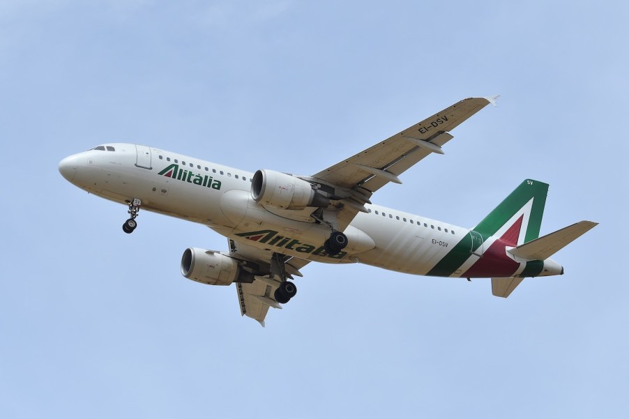 Alitalia airplane flying in front of a blue sky.