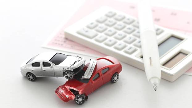 A set of tiny crashed car as an owner figures out which of the car insurance companies they'd be best to choose.