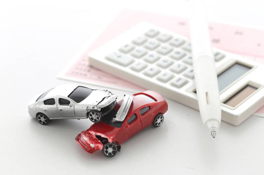 A set of tiny crashed car as an owner figures out which of the car insurance companies they'd be best to choose.