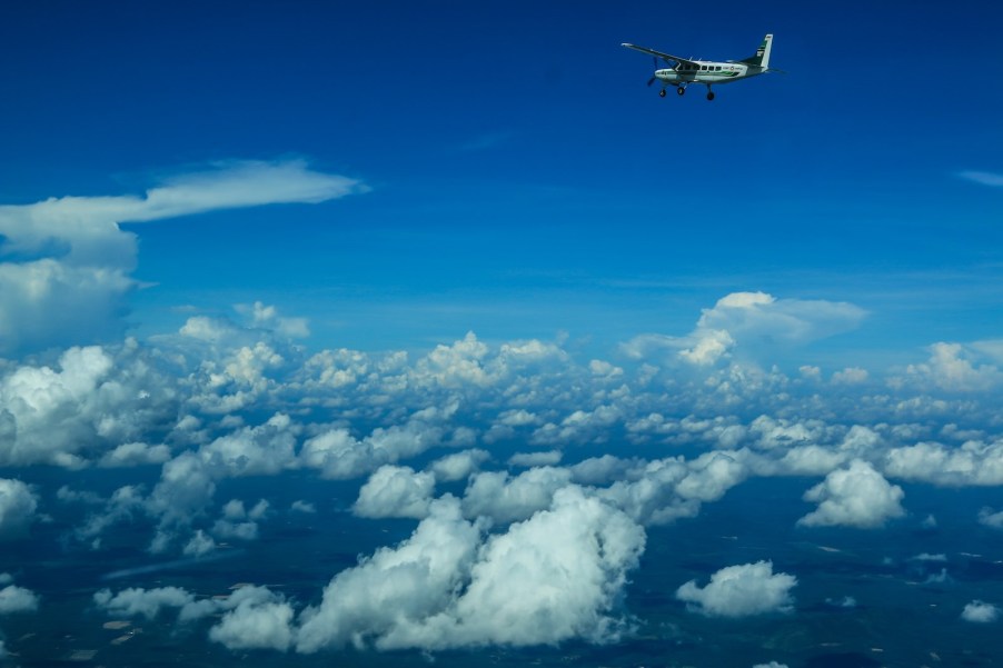 Tiny one-prop airplane flying through the sky, fluffy clouds below.