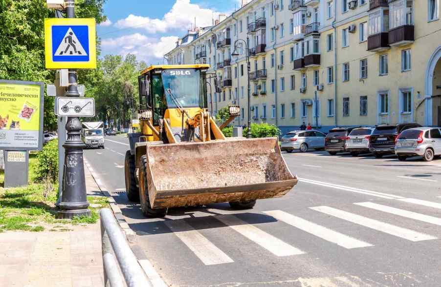 Bright yellow front-end loader driving on the road in Europe.