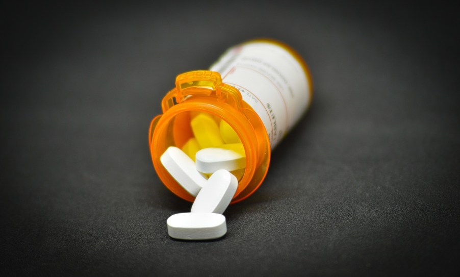 Prescription pills spilling out of an orange bottle, onto a black table