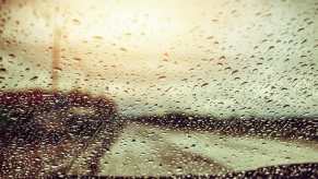 Raindrops cover the windshield of a car racing down the highway.